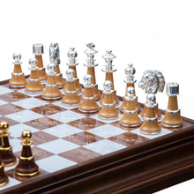 Load image into Gallery viewer, An overhead, angled view showing the smooth, brown-and-white marble grid of a chessboard flanked by silver-trimmed light wood pieces on one side and gold-trimmed dark wood pieces on the other.