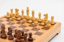 Load image into Gallery viewer, A low-angle view showing light natural wood chess pieces lined up in starting position across from dark wood pieces on an elevated wooden board.