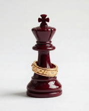 Load image into Gallery viewer, A gold textured spinner ring rests around the base of a dark maroon king chess piece.