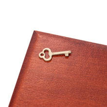 Load image into Gallery viewer, A close-up view of a small, brass skeleton key resting on the smooth, reddish-brown wooden lid of a box.