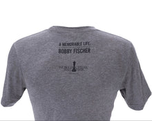 Load image into Gallery viewer, A close-up back view of the gray t-shirt displayed against a white background. Printed in dark ink on the upper back is the exhibition title, "A MEMORABLE LIFE: A Glimpse into the Complex Mind of BOBBY FISCHER," above a small chess king silhouette and the text "WORLD CHESS HALL OF FAME, Saint Louis, MO."