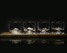 Load image into Gallery viewer, Set against a solid black background, a long wooden flight board holding four clear whiskey glasses, all mirrored perfectly on the reflective surface below. Built-in lights within the board illuminate each glass from underneath, highlighting a different intricately molded, 3D mountain peak rising up inside each base.