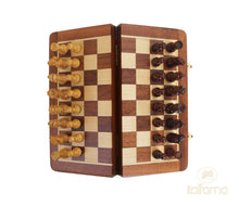 Load image into Gallery viewer, A wooden magnetic chess set with light and dark carved wooden pieces arranged on a folding checkered board with brass latches.
