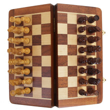 Load image into Gallery viewer, A top-down view of a open, folding wooden chessboard with carved light and dark pieces set up along its starting rows.