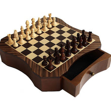 Load image into Gallery viewer, An angled view of a contoured wooden magnetic chess set fully set up with light and dark pieces, showcasing a pull-out storage drawer with a brass knob.
