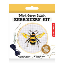 Load image into Gallery viewer, This retail box for the Kikkerland "Mini Cross Stitch Embroidery Kit" features a nature-inspired design topped with a solid, golden-yellow hanging tab. The clean white packaging prominently displays an illustration of a completed cross-stitch project showcasing a detailed black and yellow honeybee framed inside a tiny wooden hoop.