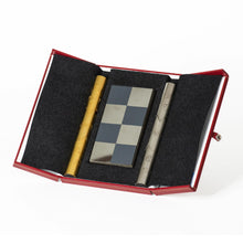 Load image into Gallery viewer, An open red leather case with a black felt interior holding a folded metal chessboard card alongside brass and silver cylindrical containers for chess pieces.