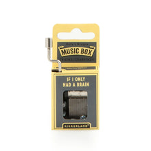 Load image into Gallery viewer, This image shows the same small, hand-cranked music box packaging, this time styled with a dark grey and pale yellow cardboard design. A silver metal crank extends from the top left side, and the front grey panel displays the text "IF I ONLY HAD A BRAIN" directly above the cutout window showing the internal metal mechanism.