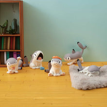 Load image into Gallery viewer, five grey-and-white Sharkitties arranged across a warm yellow wood-look floor set against a soft blue wall. The figurines are scattered near a small wooden bookshelf, with one resting on a grey mini rug.