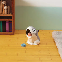 Load image into Gallery viewer, A single grey-and-white Sharkitty figurine sitting on a yellow wooden floor next to its tiny blue dish, its mouth open wide. Set in a miniature room with a wooden bookshelf on the left and the edge of a fluffy grey rug resting on the right.