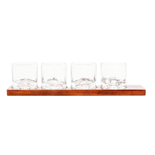 Load image into Gallery viewer, A set of four clear tumbler glasses, each featuring molded glass mountain topography inside the base, resting in a row on a long wooden serving tray.