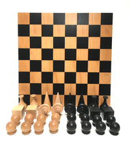 Load image into Gallery viewer, A front-facing view of light and dark geometric chess pieces grouped together in front of a upright wooden board.