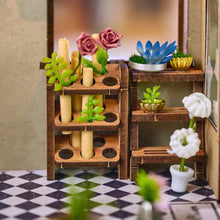 Load image into Gallery viewer, A detailed interior view highlights miniature wooden display racks holding delicate paper flowers, potted succulents, and potted white blossoms resting on a black-and-white checkered floor.