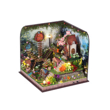 Load image into Gallery viewer, An angled front view shows an illuminated miniature fairy garden kit featuring multi-level stone staircases, small cottage structures, vibrant flora, and warm accent lighting set within a framed display.