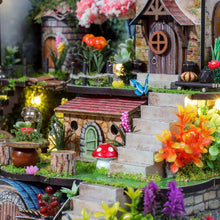 Load image into Gallery viewer, A close-up view focuses on the intricate steps, colorful artificial plants, a red-capped toadstool mushroom, and a small stone cottage entrance illuminated by soft warm light.