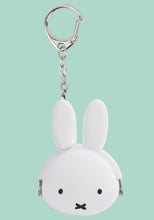 Load image into Gallery viewer, This is a small, round silicone coin purse keychain shaped like the head of the cartoon rabbit Miffy, against a mint green background. The pouch features a smooth white face with minimalist black dot eyes and a tiny "X" shaped mouth. Two long, rounded ears extend straight up from the top. A silver ball chain links the purse to a carabiner-style key clip. It uses a metal clasp hidden within the silicone frame, showing only the silver hinges on the sides.