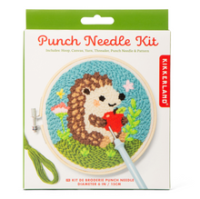 Load image into Gallery viewer, This retail package features a white box with a bright green top border that showcases a finished "Punch Needle Kit" project. The image on the packaging shows a circular wooden embroidery hoop filled with a textured yarn design of a cute hedgehog holding a bright red apple on a grassy green hill against a light blue sky.