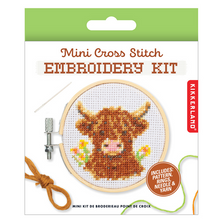 Load image into Gallery viewer, This retail package features a white card with a bright green top border that showcases a finished "Mini Cross Stitch Embroidery Kit" project. The image on the packaging shows a small circular wooden hoop framing a stitched cross-stitch design of a shaggy, brown highland cow with small yellow and orange flowers on either side.