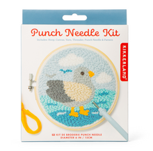 Load image into Gallery viewer, This retail package features a white box with a muted blue top border that showcases a finished "Punch Needle Kit" project. The image on the packaging shows a circular wooden embroidery hoop filled with a textured yarn design of a grey and cream Pigeon standing in bright blue ocean waves beneath a light blue sky with white clouds.