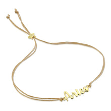 Load image into Gallery viewer, This image shows the unboxed "Aries" bracelet arranged in a loose loop against a plain white background. The delicate cursive gold nameplate rests at the bottom, while the double-strand tan cord threads through a tiny, metallic gold star-shaped slider at the top to adjust the fit.