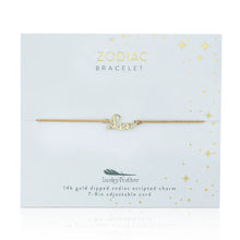 Load image into Gallery viewer, This image shows a gold "Leo" script bracelet mounted flat against a very light, ice-blue square card adorned with tiny metallic gold stars and dots. The minimalist bracelet features a delicate cursive nameplate charm dipped in 14k gold, threaded onto a thin, adjustable tan cord.