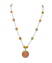 Load image into Gallery viewer, White beaded chain punctuated by faceted amber-colored glass beads, anchored by a central pendant set with an oval, shimmering orange sunstone cabochon in an ornate gold frame.
