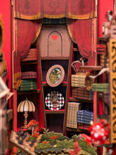 Load image into Gallery viewer, A detailed shot highlights the background alcove, featuring red draped curtains, bookshelves filled with miniature books, a framed cat portrait, a small table lamp, and red toadstools.