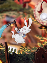 Load image into Gallery viewer, Tweezers hold a small printed wooden cutout of the White Rabbit wearing spectacles and holding a pocket watch.