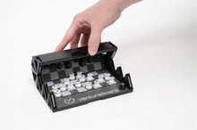 Load image into Gallery viewer, A hand begins folding a VentureBoard mini travel chess set, demonstrating how the flexible sides wrap up around the grid while keeping the pieces attached in place.