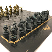 Load image into Gallery viewer, A close-up side angle of metallic gold Zelda hero pieces, including Darunia, Link, Zelda, and Navi pawns, lined up on the edge of the checkered game board.
