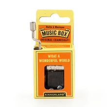 Load image into Gallery viewer, This image displays the vibrant, deep orange and yellow cardboard packaging for a Kikkerland hand-crank music box, standing vertically against a plain white background. A silver metal crankshaft handle extends upward from the top left corner, while a small rectangular window on the front reveals the inner mechanical music parts directly beneath the printed song title, "WHAT A WONDERFUL WORLD."
