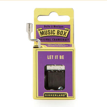 Load image into Gallery viewer, This image displays the vibrant purple and yellow cardboard packaging for a Kikkerland hand-crank music box against a plain white background. A silver metal crankshaft handle extends upward from the top left corner, while a small rectangular window on the front reveals the inner metal mechanism right below the printed song title, "LET IT BE."
