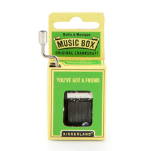 Load image into Gallery viewer, This image displays the bright green and yellow cardboard packaging for a Kikkerland hand-crank music box, standing vertically against a plain white background. A silver metal crankshaft handle extends upward from the top left corner, while a small rectangular window on the front reveals the inner mechanical music parts directly beneath the printed song title, "YOU'VE GOT A FRIEND."
