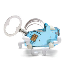 Load image into Gallery viewer, This image presents the mechanical wind-up toy standing on its white plastic feet against a stark white background. Viewed from the side, its chassis is made of glossy, bright blue metal that showcases a brass-colored gear on its flank, a large silver winding key protruding from the back, and arched metal ribbon springs curving over its top.
