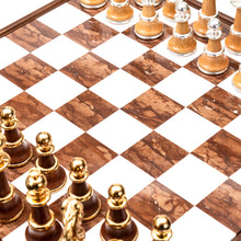 Load image into Gallery viewer, A close-up side view of a polished marble chessboard displaying light wood chess pieces with silver accents lined up opposite dark wood pieces with gold accents.
