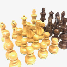 Load image into Gallery viewer, A close-up perspective view of carved light and dark wooden Staunton chess pieces lined up on a white surface.
