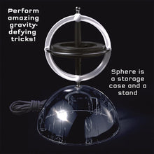 Load image into Gallery viewer, This image highlights the gyroscope toy balancing upright on a curved, clear plastic dome that serves as both a storage case and a tabletop stand. The gyroscope itself consists of a central, heavy black disc wrapped in a white circular frame, with a metal axis pinning it through the middle and tapering into small metallic balls at each tip.
