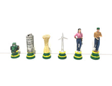 Load image into Gallery viewer, A line of farm-themed chess pieces on green-and-yellow bases including a tractor, silo, wheat sheaf, wind turbine, female farmer, and male farmer holding a shovel.
