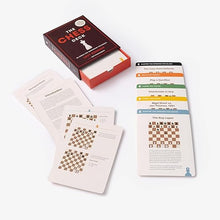 Load image into Gallery viewer, The open card box sitting on a white background next to various included instructional cards displaying chess diagrams and text.
