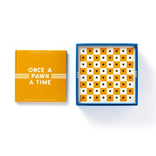 Load image into Gallery viewer, A yellow hardcover instruction book titled "ONCE A PAWN A TIME" sits next to a blue box containing a yellow-and-white perforated peg-style chessboard.
