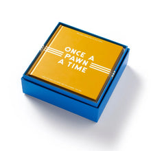 Load image into Gallery viewer, A yellow hardcover instruction book titled "ONCE A PAWN A TIME" resting inside a blue storage box.
