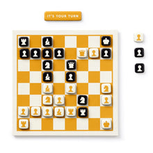 Load image into Gallery viewer, A yellow-and-white magnetic chessboard set up with square black and cream piece magnets during a game, accompanied by an "IT'S YOUR TURN" magnetic marker.
