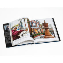 Load image into Gallery viewer, Displaying a two-page spread about chess in Saint Louis. On the left page, a man wearing sunglasses and a burgundy jacket plays chess outdoors with a glass of wine nearby, while the right page features the world's largest chess piece standing outside the World Chess Hall of Fame and Galleries building.
