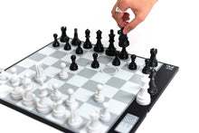 Load image into Gallery viewer, A person's hand reaches down to lift a black knight during a game played on the DGT Centaur digital chessboard.
