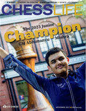 Load image into Gallery viewer, Front cover of the November 2023 issue of Chess Life magazine, featuring a smiling GM Abhimanyu Mishra raising his arms in celebration in front of a giant wooden chess king sculpture and a brick building.
