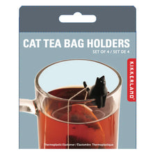 Load image into Gallery viewer, This retail blister pack for Kikkerland "Cat Tea Bag Holders" features a muted greyish-blue background topped with a solid dark grey hanging tab. The packaging displays a close-up photo of a clear glass mug filled with amber tea, showcasing a tiny, black plastic cat figure perched on the rim with a tea bag string wrapped around its tail.
