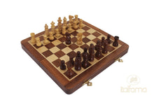 Load image into Gallery viewer, A wooden magnetic chess set with light and dark carved wooden pieces arranged on a folding checkered board with brass latches.
