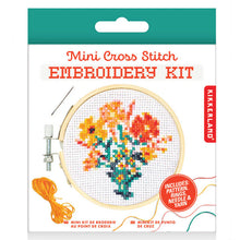 Load image into Gallery viewer, This retail box for the Kikkerland "Mini Cross Stitch Embroidery Kit" features a floral design topped with a solid teal-green hanging tab. The white packaging prominently displays an illustration of a completed cross-stitch project showcasing a colorful bouquet of orange and yellow flowers in a small vase, all framed inside a tiny wooden hoop.
