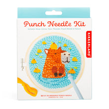 Load image into Gallery viewer, This retail box for a Kikkerland "Punch Needle Kit" features an animal theme and is topped with a bright, light blue hanging tab. The clean white packaging prominently displays an illustration of a textured, completed project showcasing a brown capybara with a small yellow bird on its head, all set against a vibrant turquoise background and framed inside a six-inch wooden hoop.
