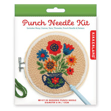 Load image into Gallery viewer, This retail box for a Kikkerland "Punch Needle Kit" features a vibrant floral theme and is topped with a solid green hanging tab. The clean white packaging prominently displays an illustration of a textured, completed project showcasing a variety of red, blue, and orange flowers arranged inside a dark blue patterned teapot, all set against a neutral beige background and framed in a six-inch wooden hoop.
